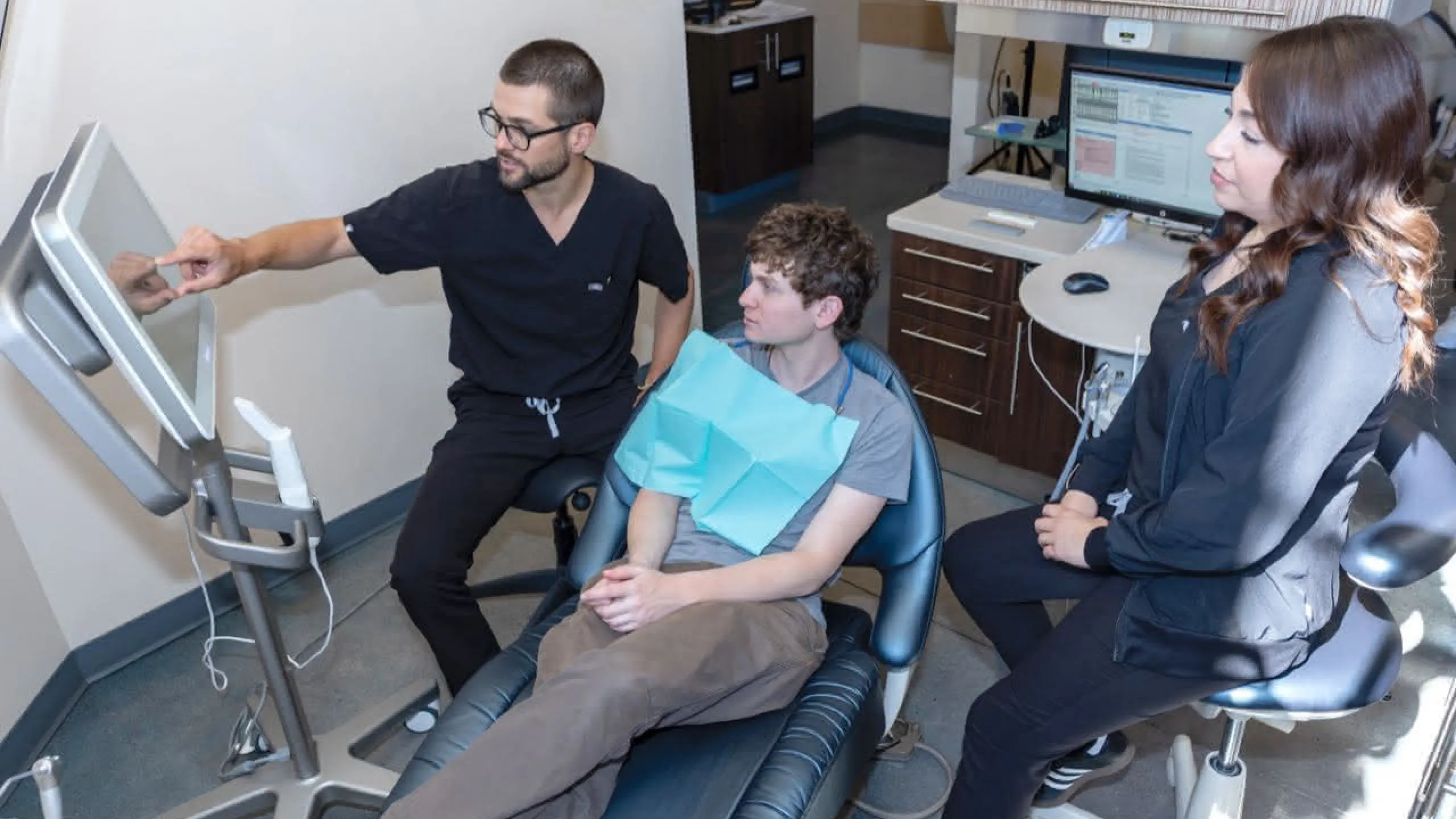 A doctor pointing at a monitor with a patient in a chair