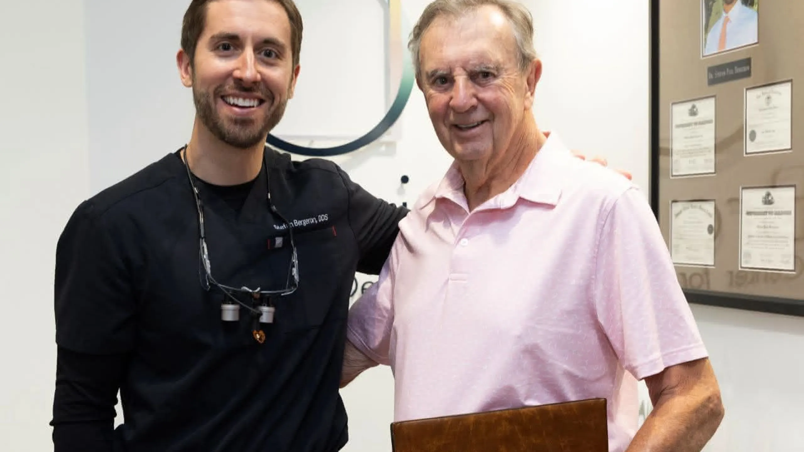 A dentist with a patient in a pink shirt holding a folder