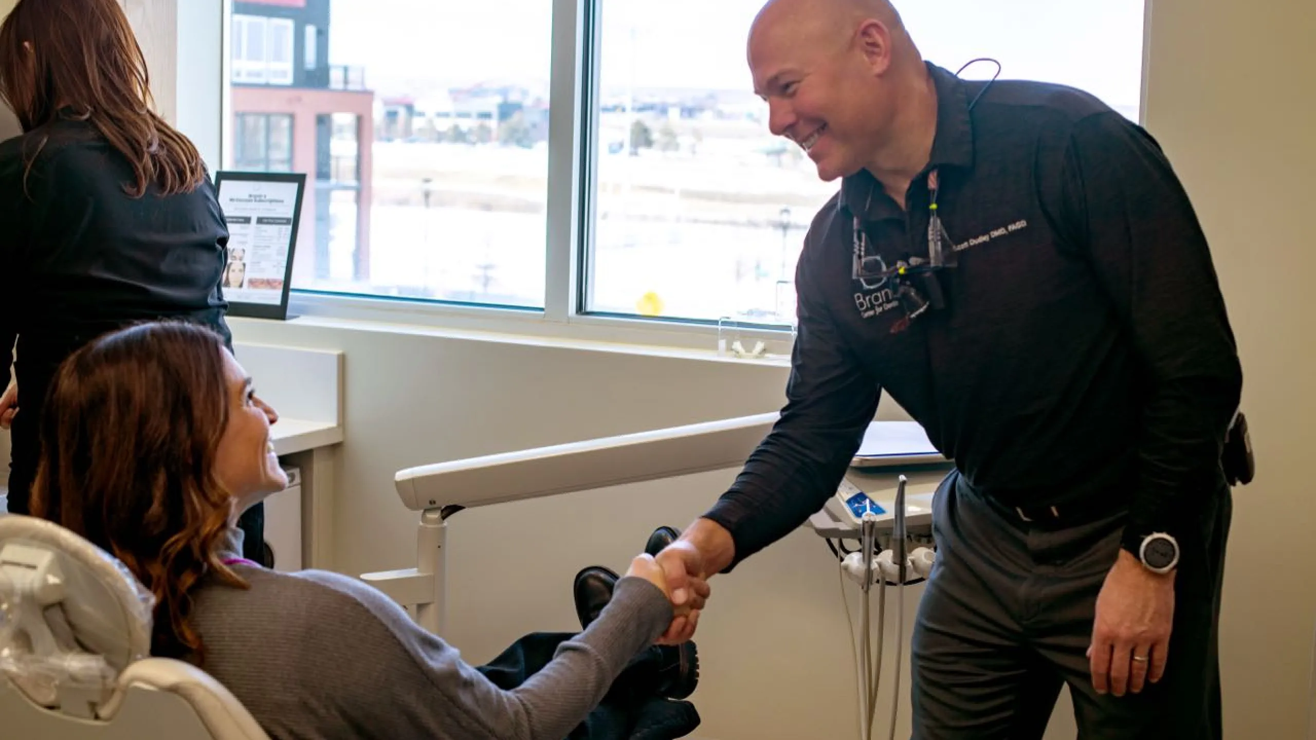 A patient in an exam chair shaking hands with Dr. Dudley