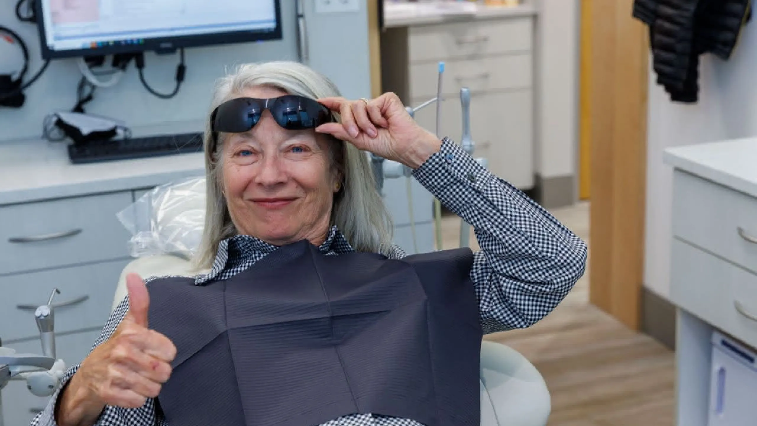 A patient lifting a pair of sunglasses giving a thumbs up