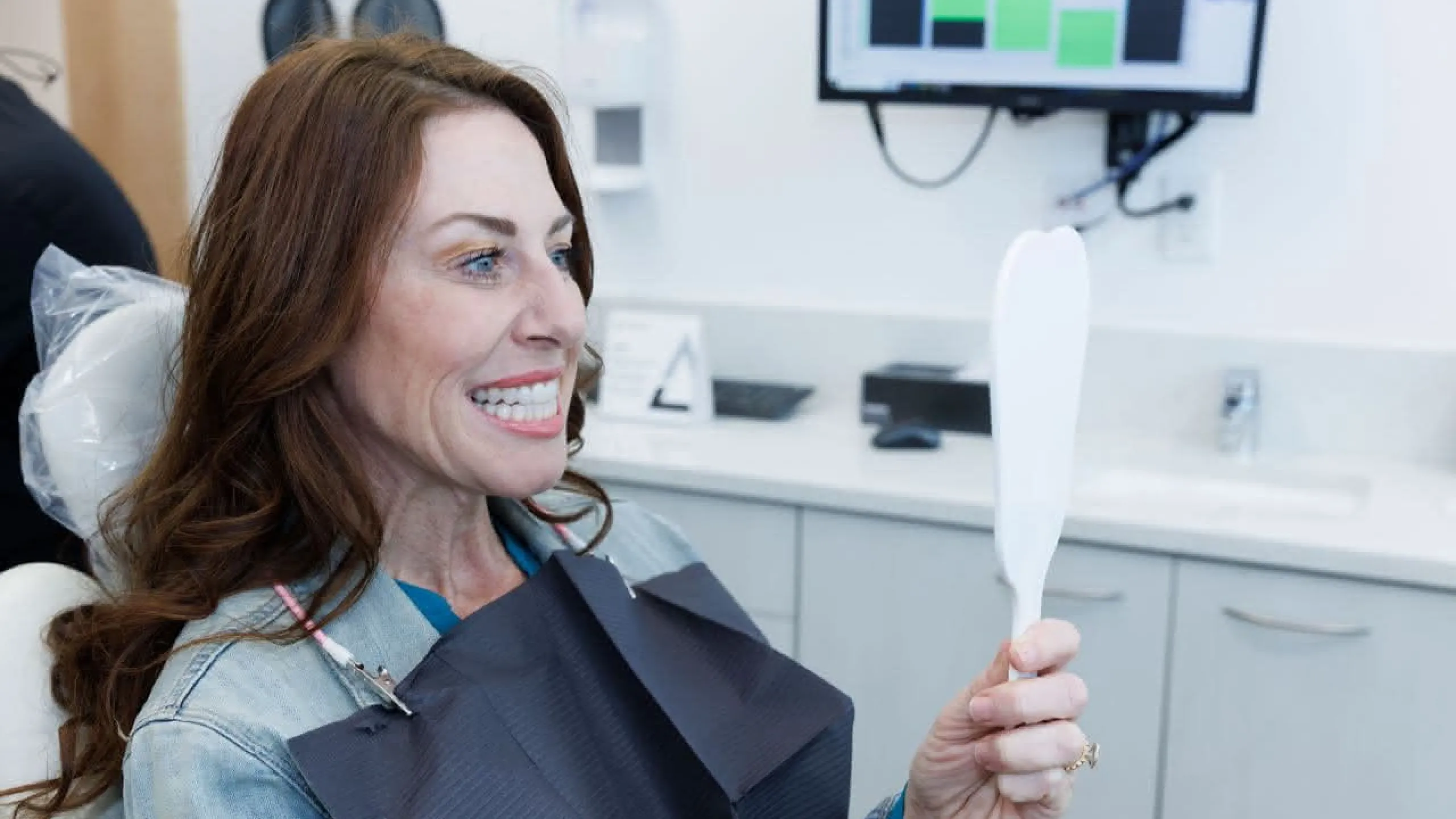A patient holding a hand mirror smiling
