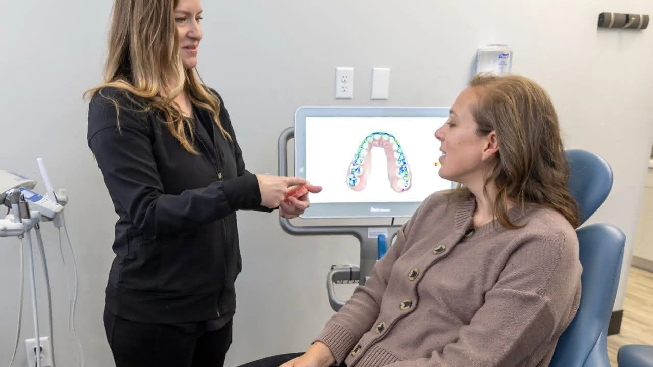 A dental assistant show a patient an example in front of an X-ray