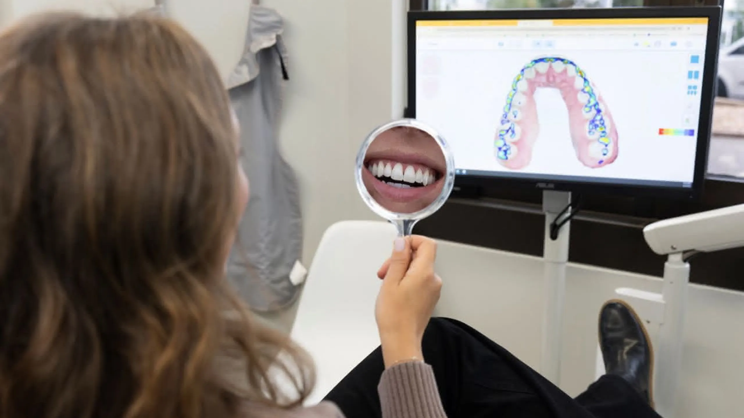 A patient holdind a hand mirror in front of a computer