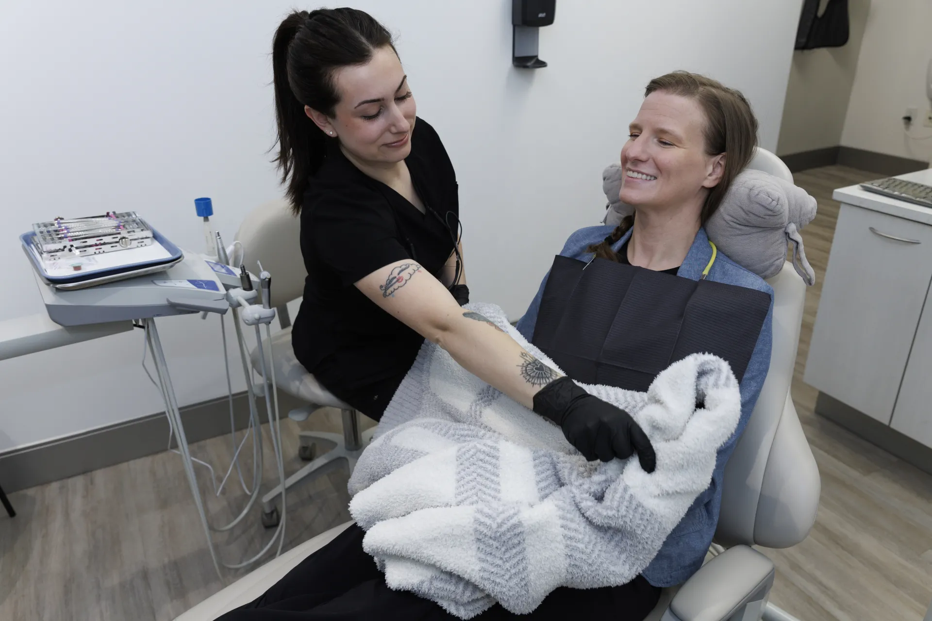 A dental assistant placing a blanket on a patient to keep cozy
