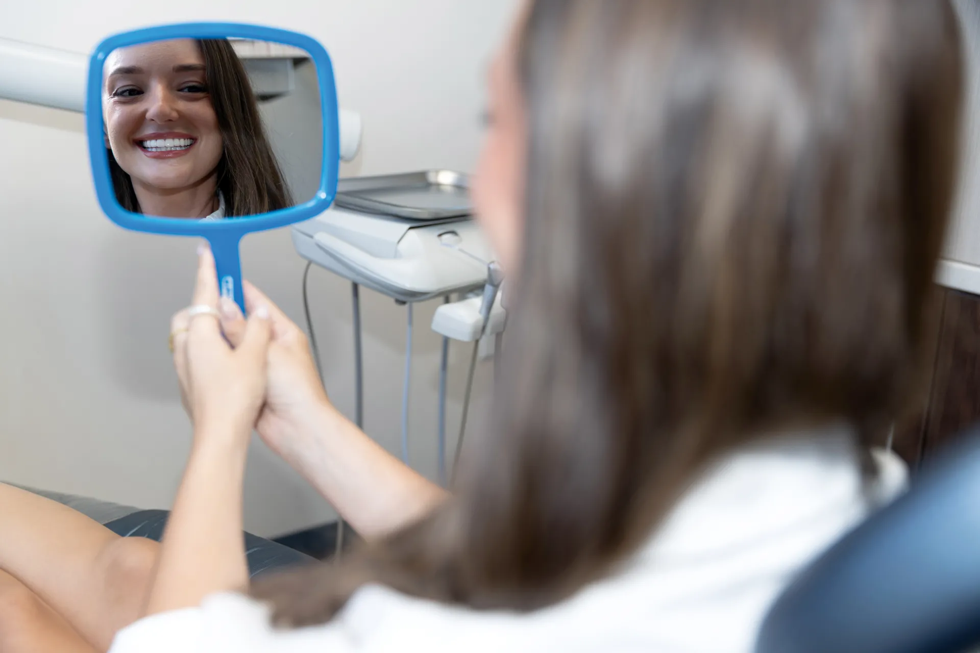 A happy patient smiling in a blue hand held mirror showing her beautiful smile!