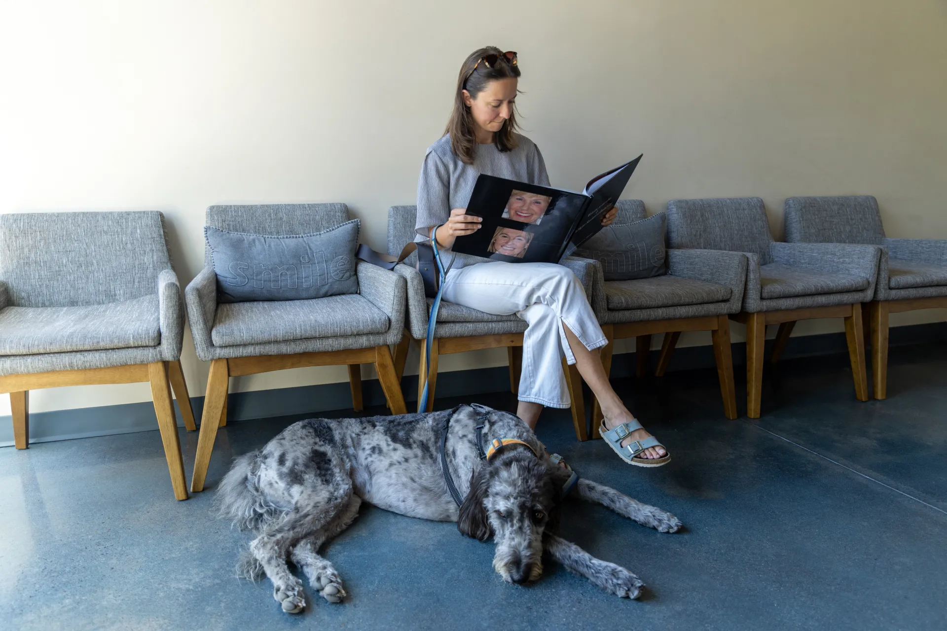 A patient sitting in the waiting room reading a book with her dog laying at her feet