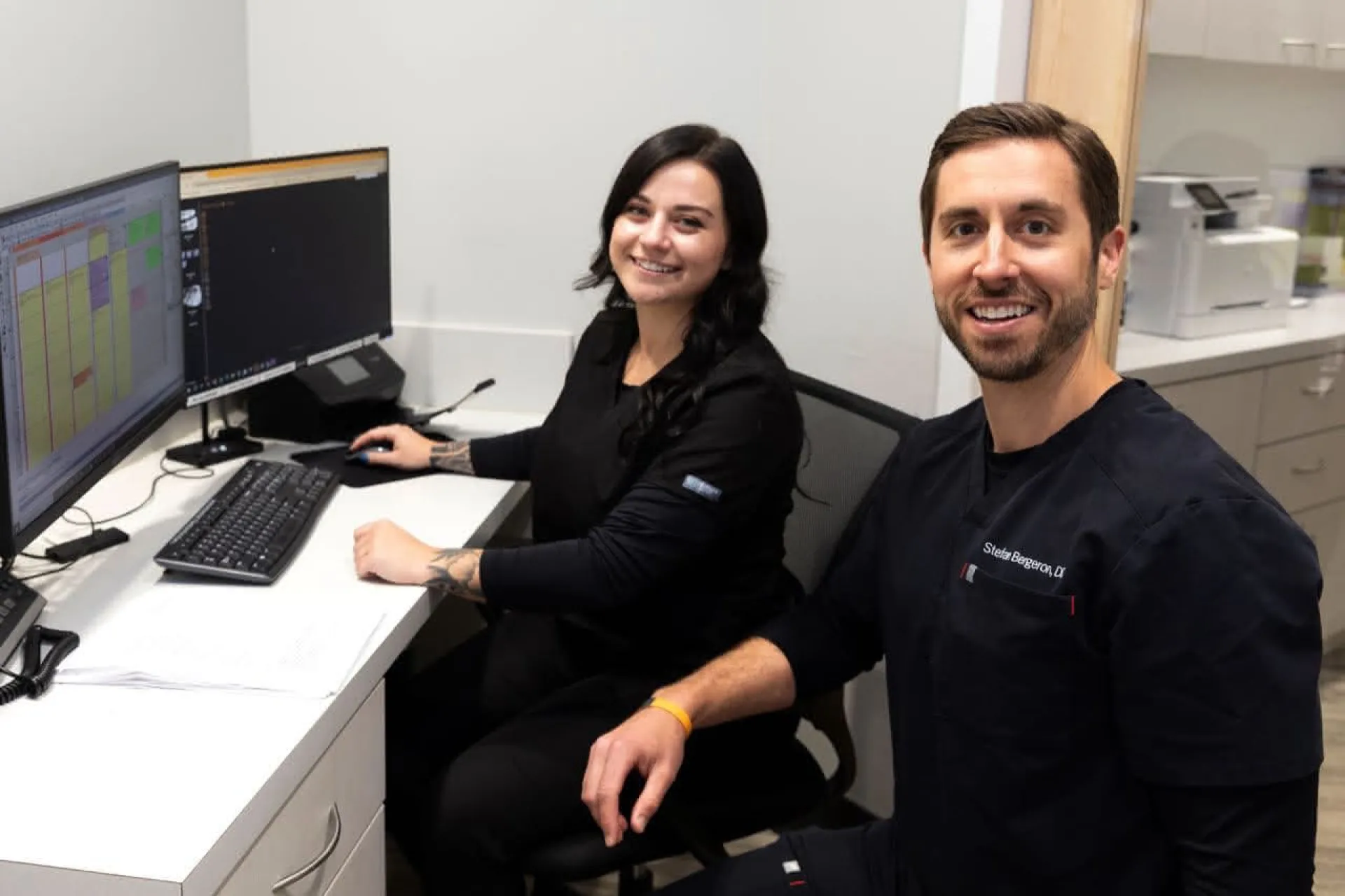 A dental assistant at a computer with a dentist off to the side