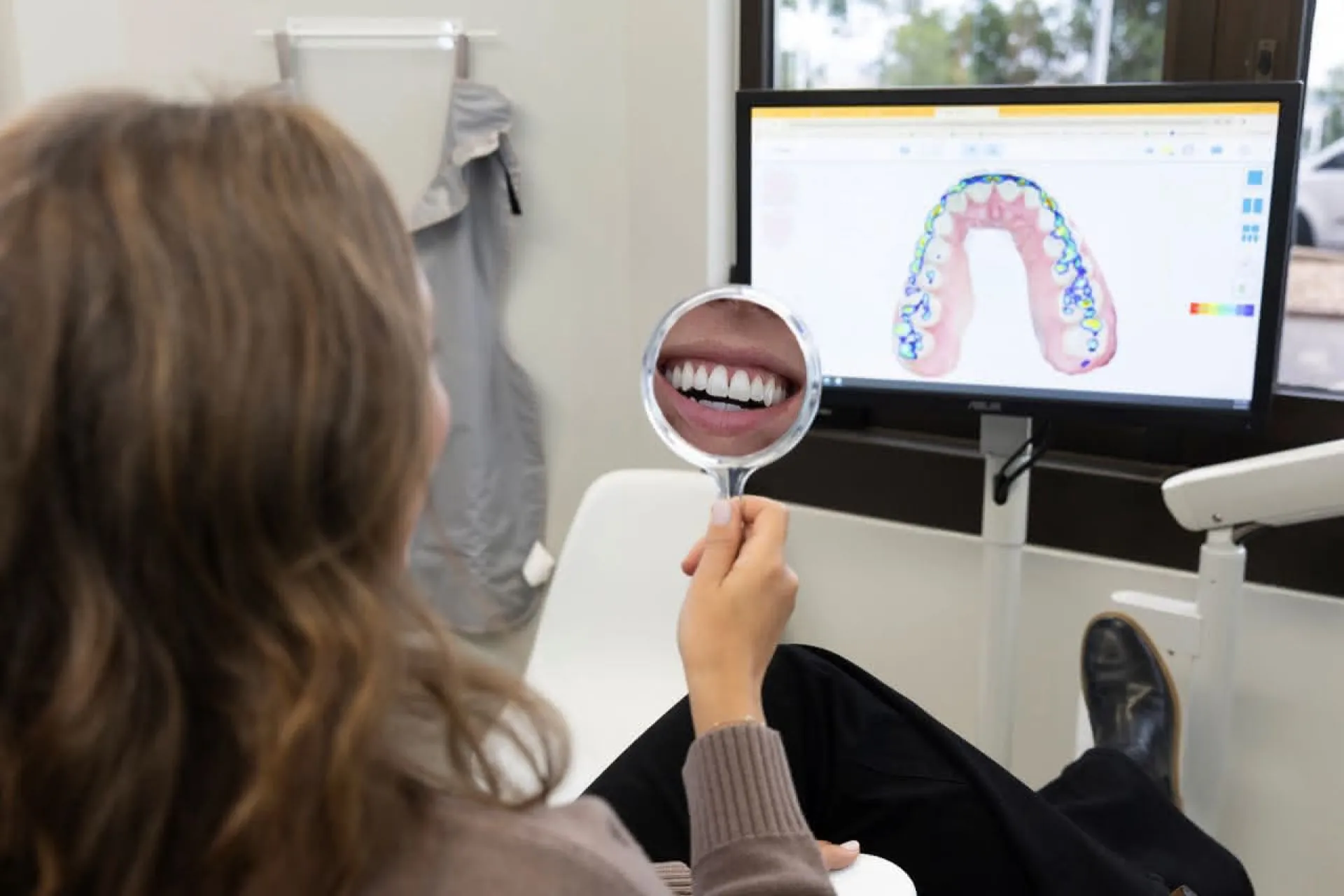 A patient holdind a hand mirror in front of a computer