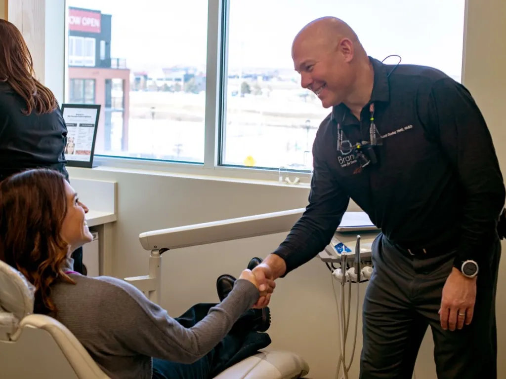 A patient in an exam chair shaking hands with Dr. Dudley