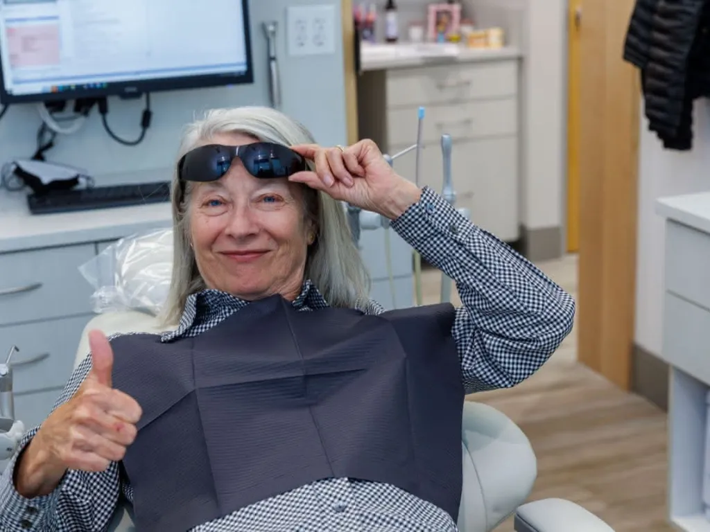 A patient lifting a pair of sunglasses giving a thumbs up