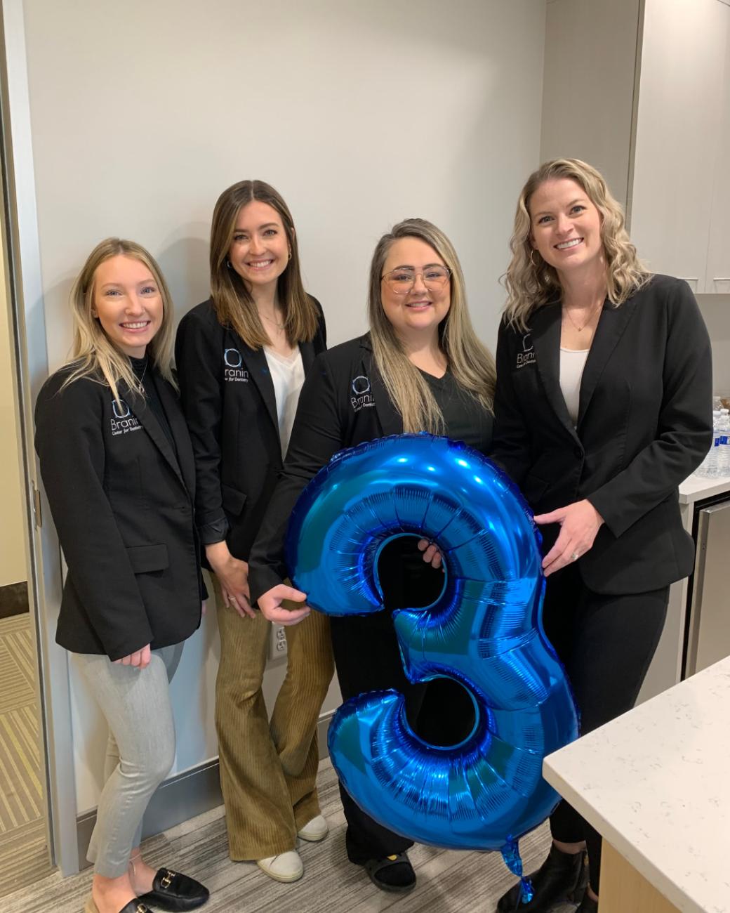 Team members holding a balloon shaped like a number three