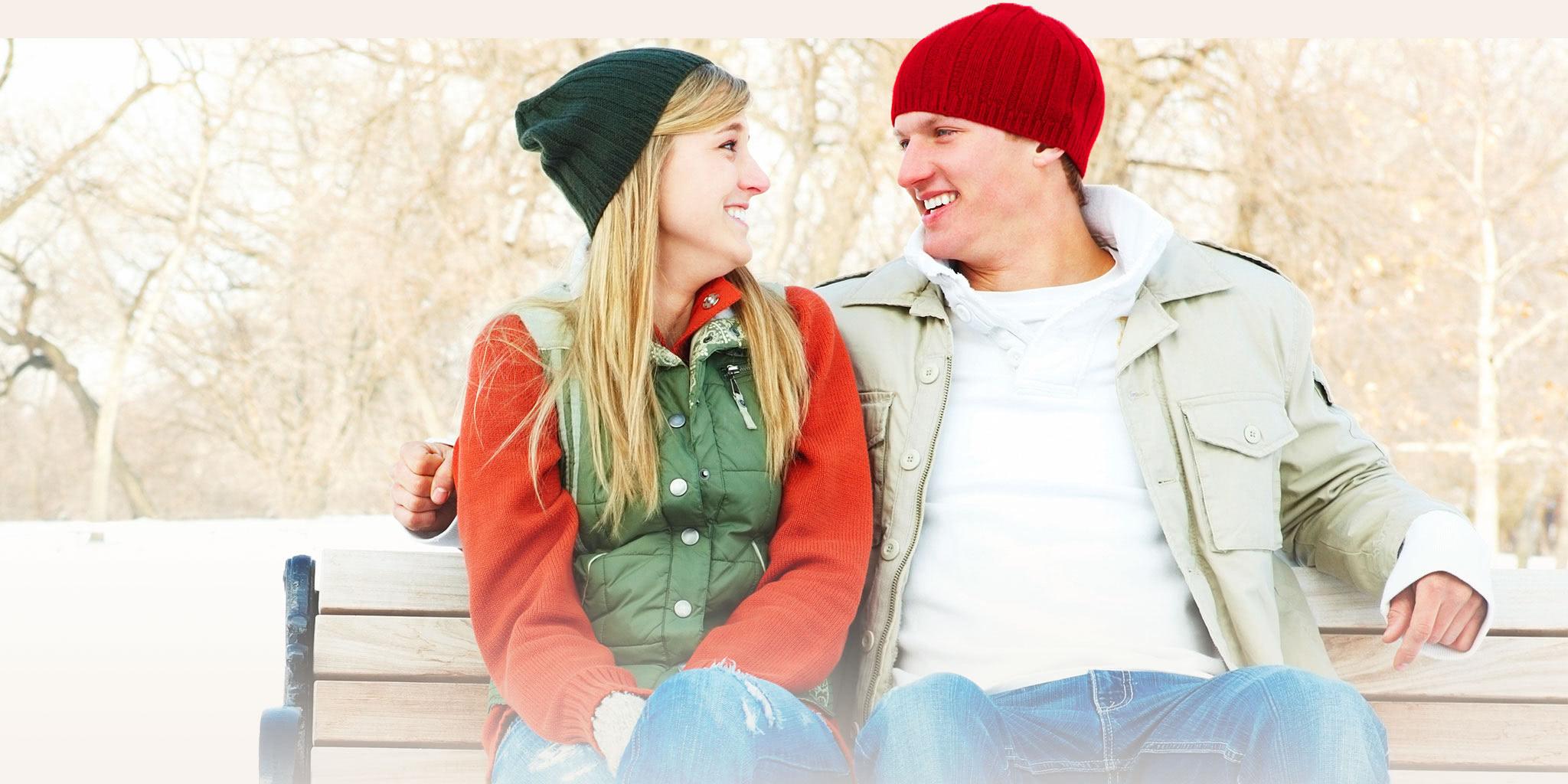 A couple on a bench in winter with stocking caps on