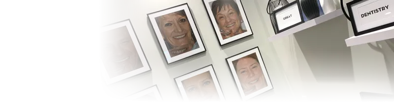 Small frames with the words Great and Dentistry on shelves in front of a wall with smile gallery portraits.