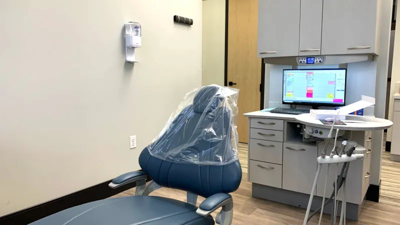 A blue dentist chair with striped wood floor and white walls